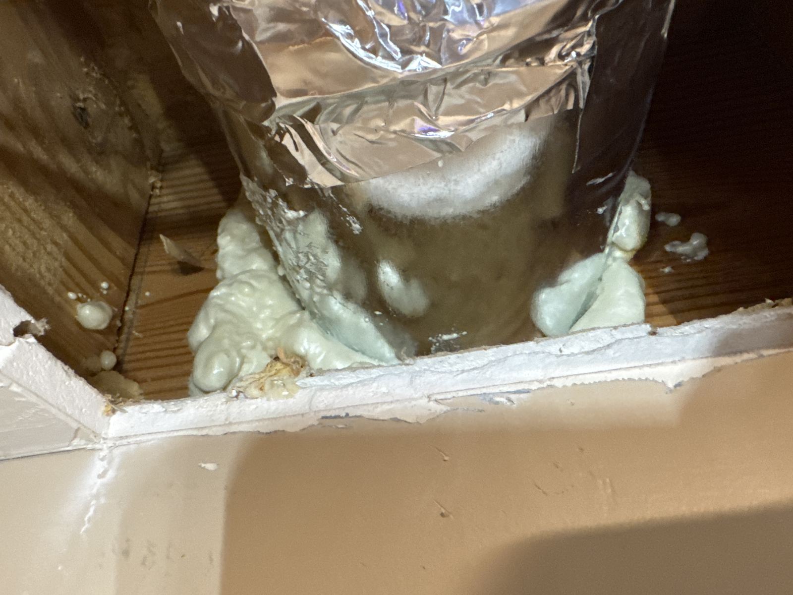 Range hood exhaust duct sealed with foam insulation at the ceiling
