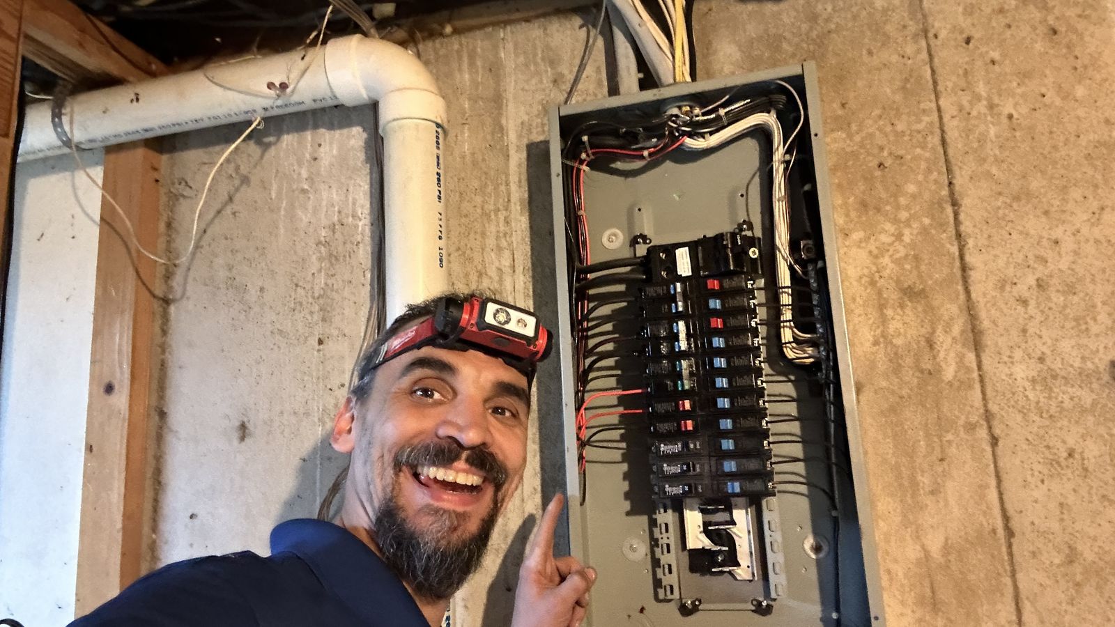 Gabriel next to an open breaker panel in a basement