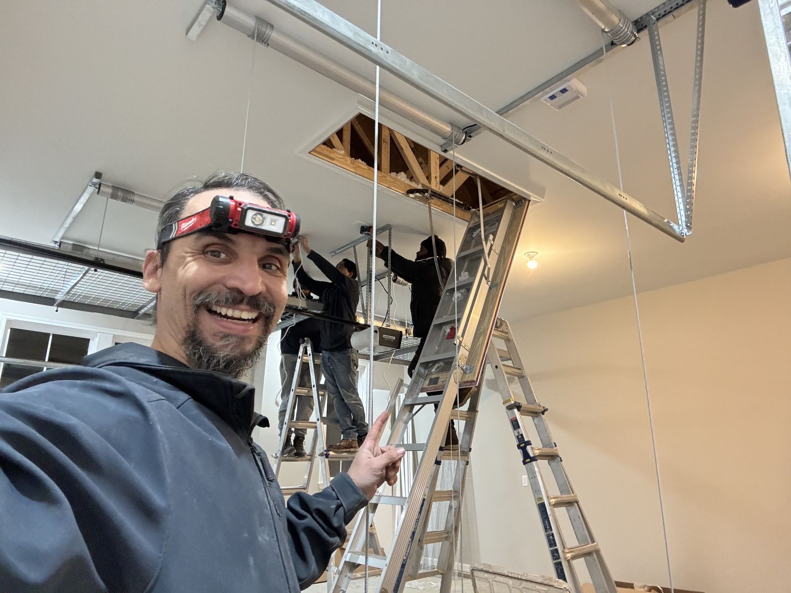 Gabriel installing a high-ceiling light fixture from ladders