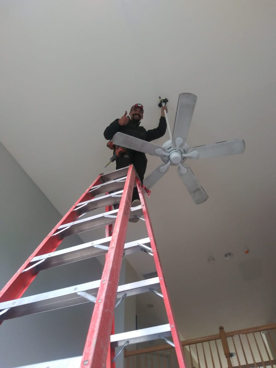 Ceiling fan installation on a tall ladder in a high ceiling